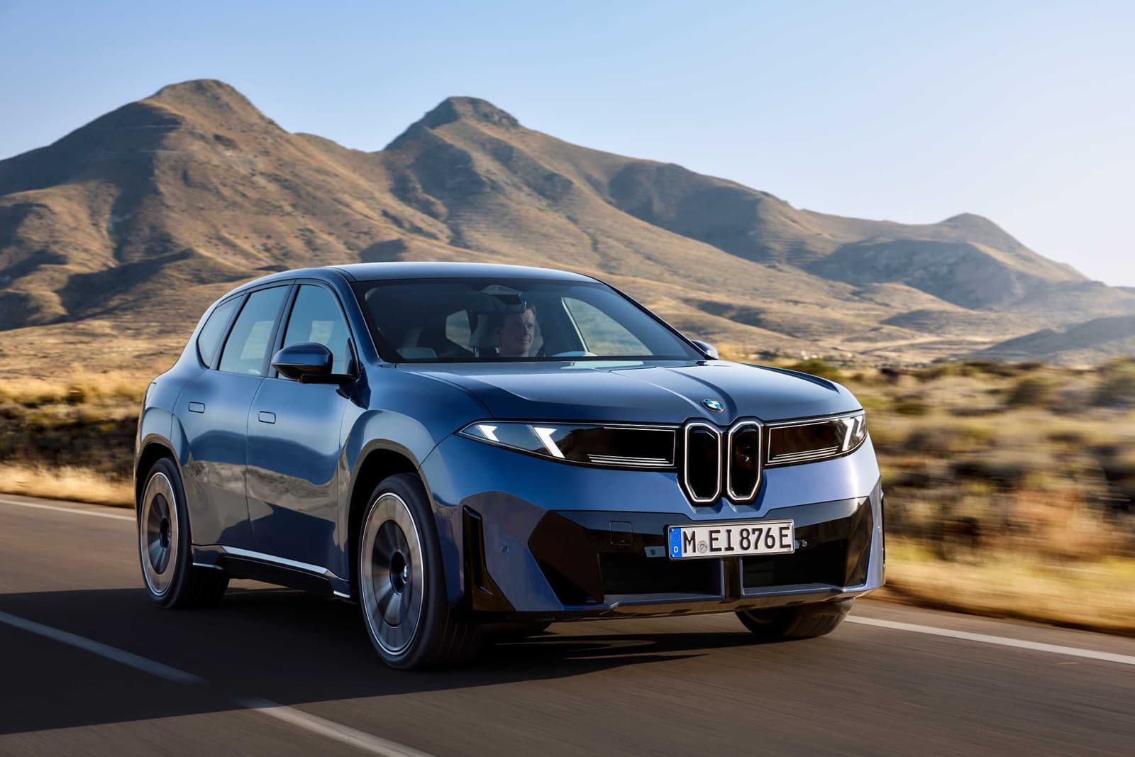 Blue BMW iX3 50 xDrive driving on a road lined with mountains