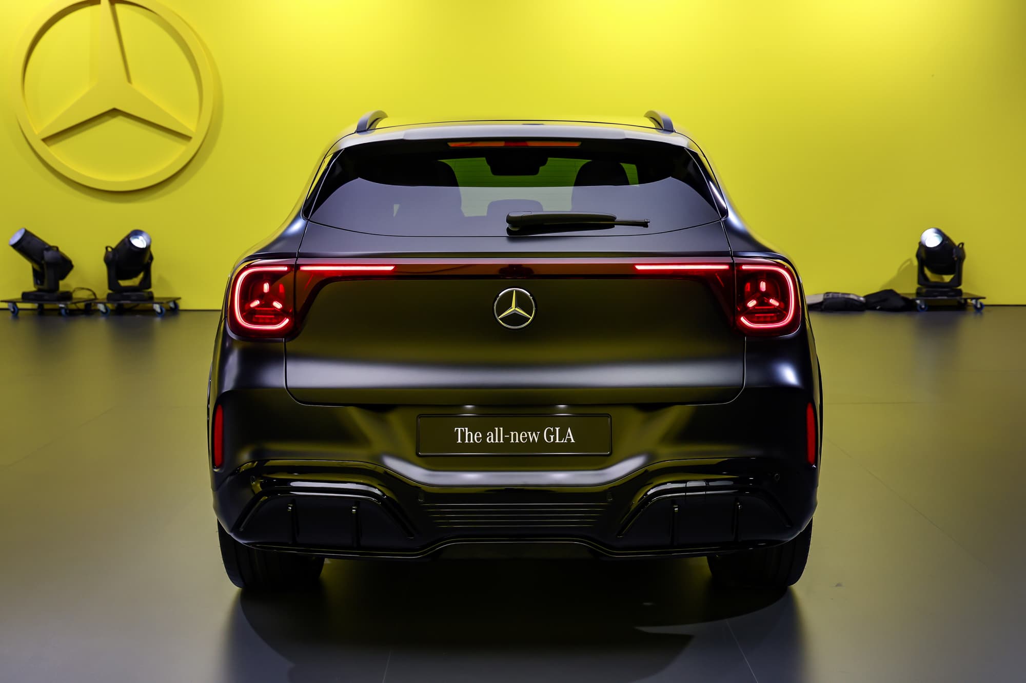 The new GLA seen from behind on a launch stage, red light bar lit, yellow backdrop with the Mercedes star