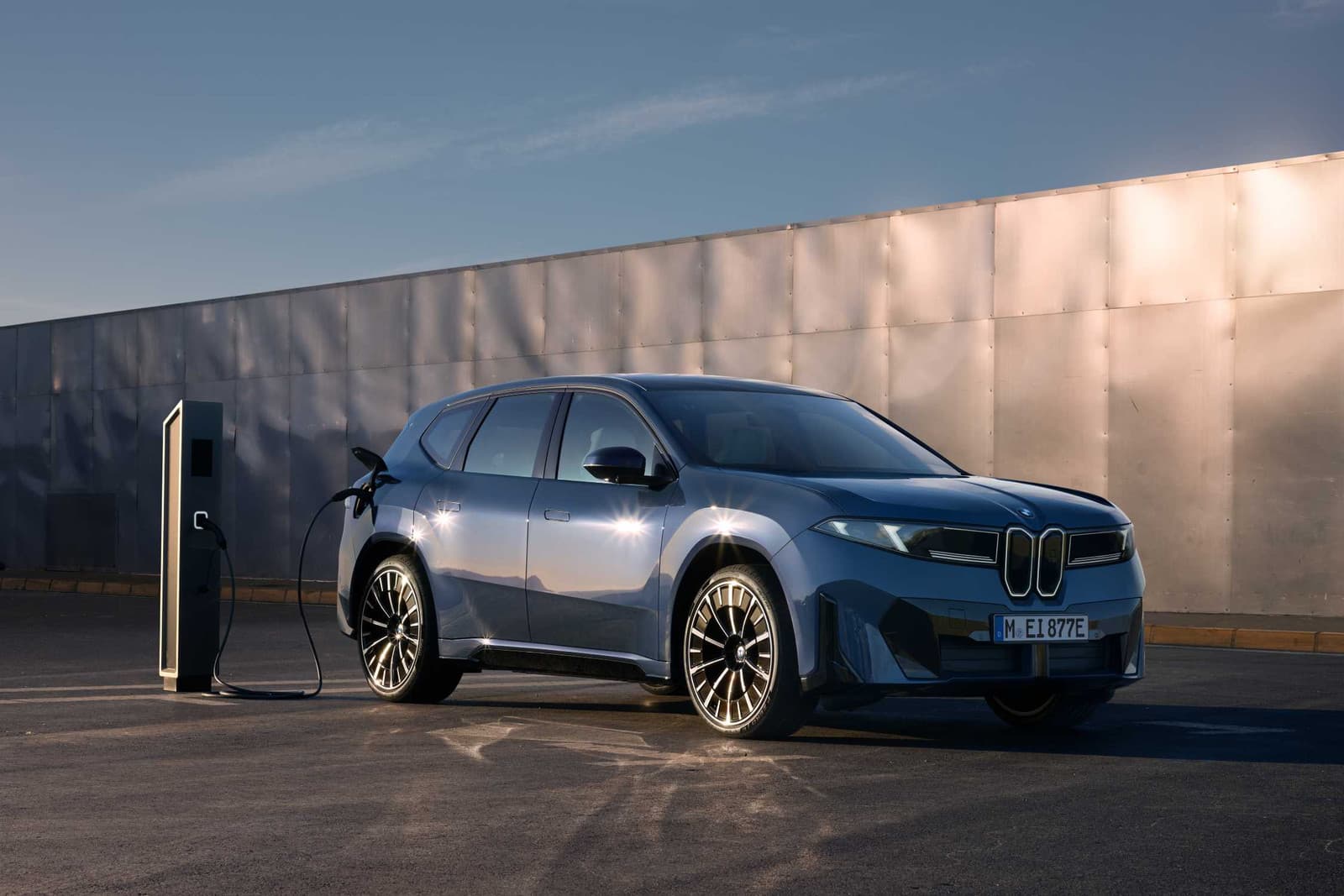 BMW iX3 charging at a rapid charger, parked in front of a metal wall